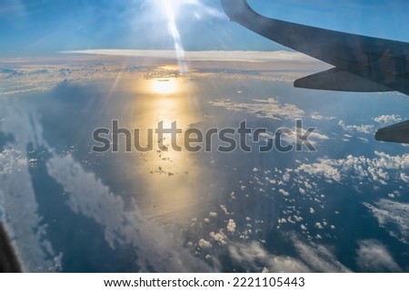Airplane flies over the Atlantic Ocean during sunrise. View from the plane window on the orange reflection of the sun in the blue water under the clouds
