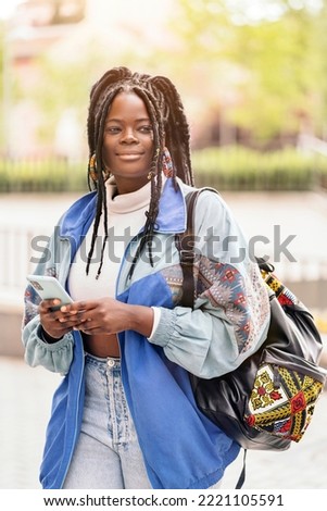 Happy african woman with cool braids walking in the street and using her mobile phone.