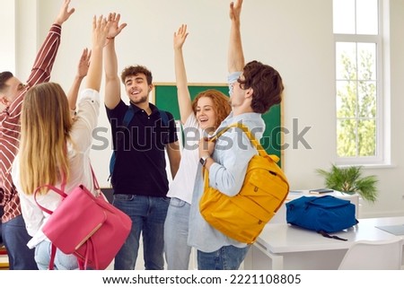 Intelligent High school students rise hands up at modern classroom with green chalkboard on background. Celebration of successfully passed exams, well-done creative work, week end or vacation. Royalty-Free Stock Photo #2221108805