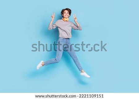 Full body photo of short hairdo young lady jump wear headphones shirt jeans sneakers isolated on blue color background