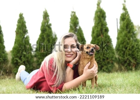 A girl with her pet girl on the grass. A blonde with her little chihuahua lies on the green grass in the yard. An attractive, young, blonde girl with a small brown dog in her arms.