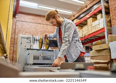 Side view portrait of young man setting up roller printing machine in industrial shop, copy space