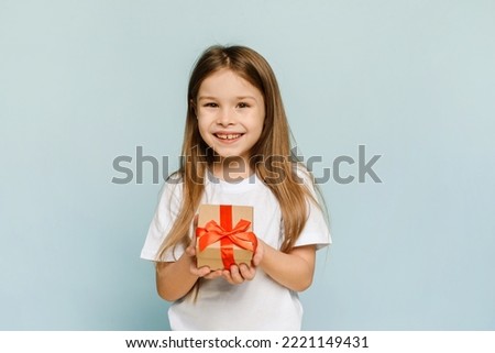 A female child holds a box with a Christmas present in her hand. Isolated on blue background
