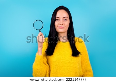 Photo of cute smart young lady working as detective find clues with magnifier glass isolated on blue color background
