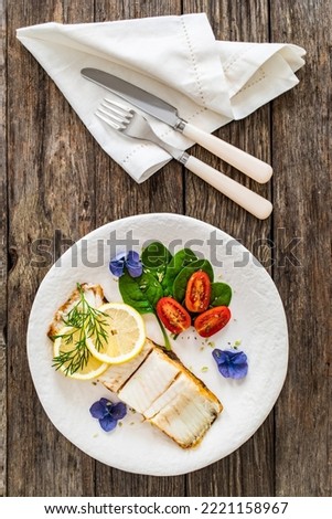 Fish dish - fried halibut with lemon and fresh vegetables on wooden table 