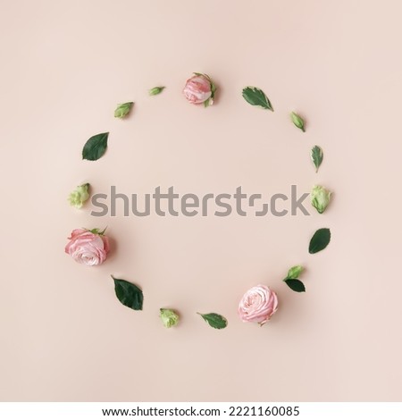 Natural round frame with copy space made of flowers and leaves on trendy pastel beige background. Roses and small buds making abstract composition with space for design. Easter, spring concept