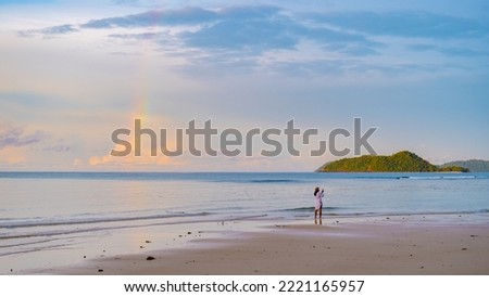 Asian women looking at a rainbow on the beach after a monsoon rain storm in Thailand.Asian women walking on the beach of Koh Mak during sunrise Royalty-Free Stock Photo #2221165957