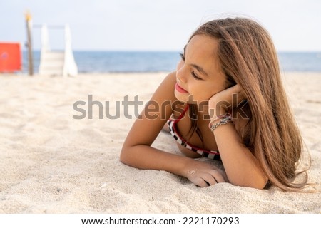 Little beautiful smiling girl lying on the sand at the beach.