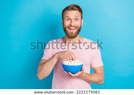 Photo of funny impressed guy dressed pink t-shirt eating pop corn watching interesting movie isolated blue color background