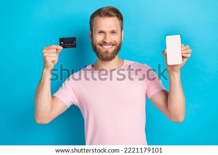 Photo of positive pretty guy dressed pink t-shirt rising credit card modern gadget empty space isolated blue color background