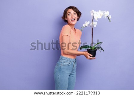 Photo portrait of cute young lady hold orchid look excited empty space dressed stylish striped clothes isolated on purple color background