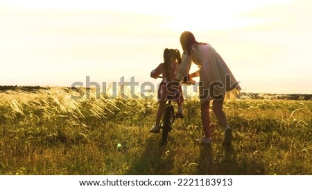 mother teaches little child daughter ride bike park sunset. cycling kid with parent outdoors. happy family. mother daughter play with bicycle nature. happy family concept. chidhood dream. weekend. Royalty-Free Stock Photo #2221183913