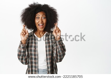 Hopeful african woman wishing, cross fingers for good luck and smiling, anticipating smth, yearning and begging, standing over white background