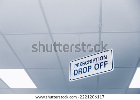 Plain white and blue prescription drop off sign hanging from a ceiling with copyspace inside a drugstore.