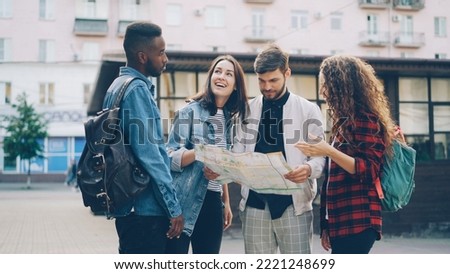 Young men and women with backpacks are looking at paper map standing in the street in foreign city and talking discussing journey. Navigation, youth and tourism concept.