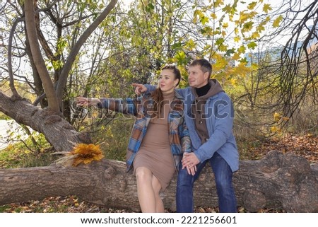 A married couple waiting for a baby sit on a branch in the park.