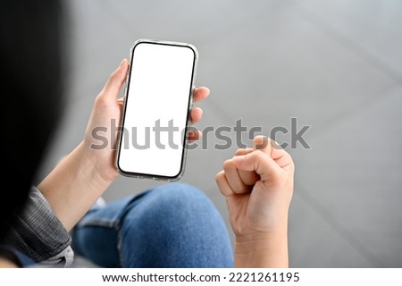 A female hand holding a smartphone white screen mockup and showing clenched fist. winning, victory, yes, success pose. close-up image
