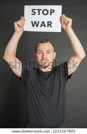 Young handsome man holds stop war sign under his head on dark background