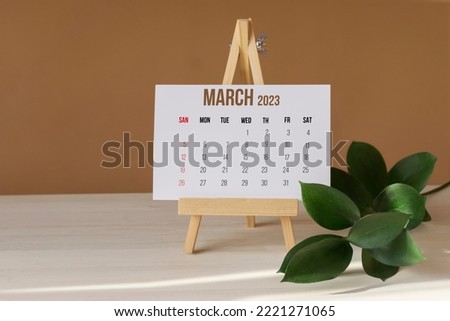 March 2023. Calendar for month on wooden stand. Sheet of white paper with days and weeks on desktop next to green branch. Concept of New Year Royalty-Free Stock Photo #2221271065