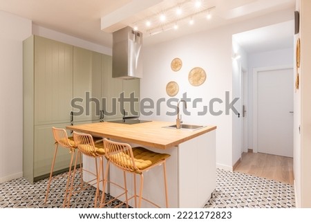 Bright warm kitchen with appliances, wooden island and high chairs in modern apartment