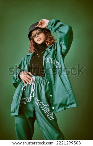 Fashion clothes, style and black woman with green rap, gen z or hip hop aesthetic outfit for cool, edgy or fashionable look. Designer brand apparel, attitude or teen fashion model on green background Royalty-Free Stock Photo #2221299503