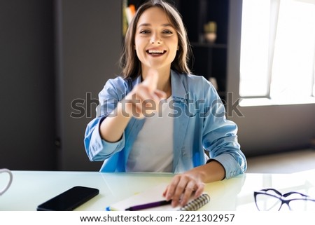 Portrait of young woman sitting looking at her laptop screen on video call, pointing on office background.
