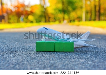 Aviation industry and ecology related mock-up: toy aircraft placed on green wooden letter blocks.