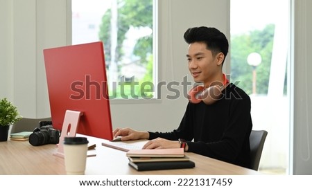 Smiling asian male photo editors retouching photos on personal computer, working in creative office