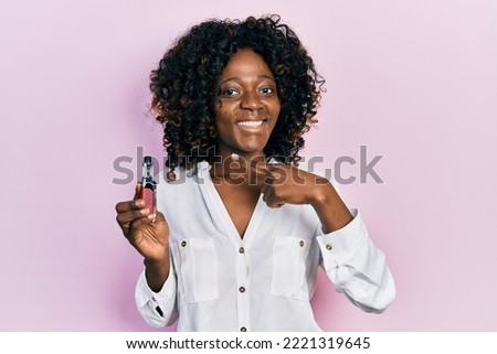 Young african american woman holding electronic cigarette smiling happy pointing with hand and finger 