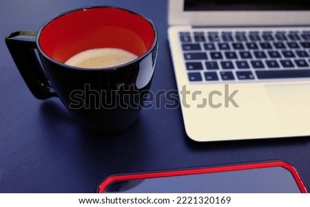 A working place with laptop, smartphone and black and red mug with coffee