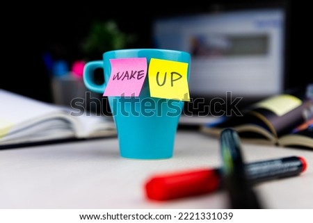 Sticky notes on a coffe cup at office desk. Wake up. Prepare for work