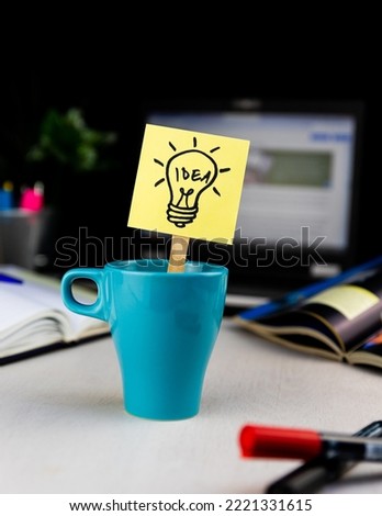 Light bulb doodle drawn on sticky note inside a cup of coffee at the office desk. Ideas, inspiration and creative thinking comes with a morning cup of coffee.