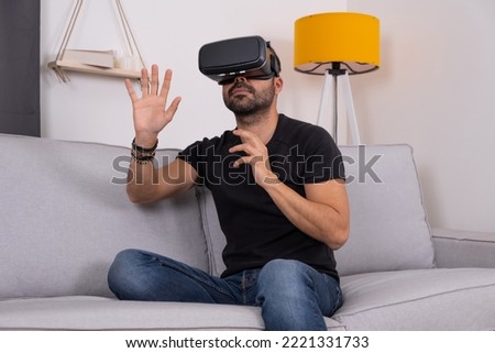Young man using VR glasses headset at home gesturing. Virtual reality, future technology, education video gaming.