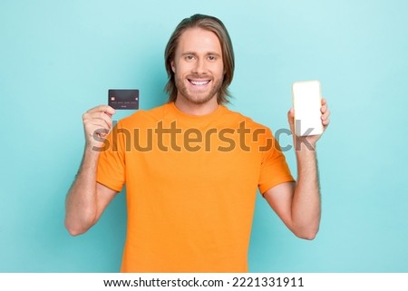 Photo of cheerful funky guy dressed orange t-shirt rising credit card modern device empty space isolated teal color background