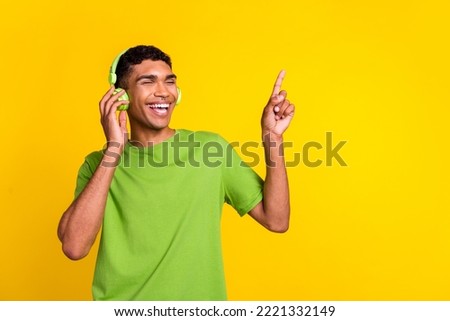 Photo portrait of handsome young man touch earphones have fun enjoy melody wear stylish green outfit isolated on yellow color background