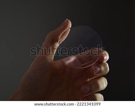 Glass lens for eyewear, hand holds a circular lens for eyewear manufacturing Royalty-Free Stock Photo #2221341099