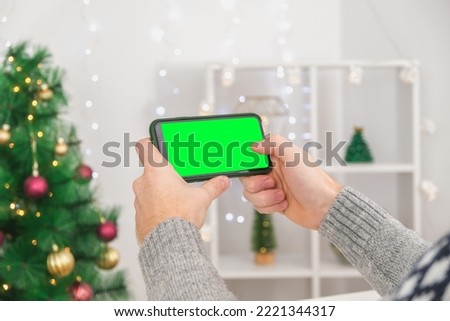 A man holds a phone in a horizontal position with a green screen. Phone with chromakey. Copy space. The concept of advertising, New Year's holidays, Christmas.