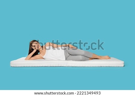 Young woman lying on soft mattress against light blue background