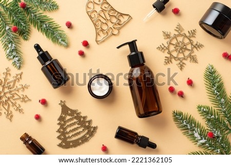 Winter skin care concept. Top view photo of amber glass bottles without label cream jar christmas tree ornaments mistletoe berries fir branches in frost on isolated beige background with empty space