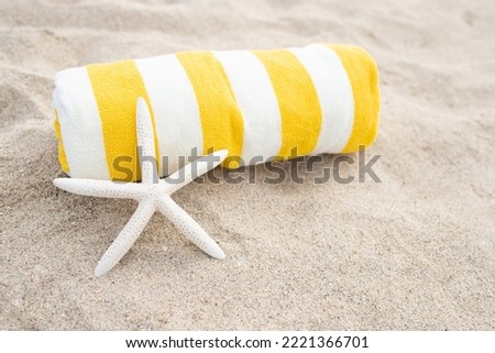 Rolled up striped white and yellow towel, white starfish shell on the sandy beach. Sunny day. The concept of tanning, vacation, relaxation, retreat, vacation, travel, sunbathing. Copy space. Royalty-Free Stock Photo #2221366701