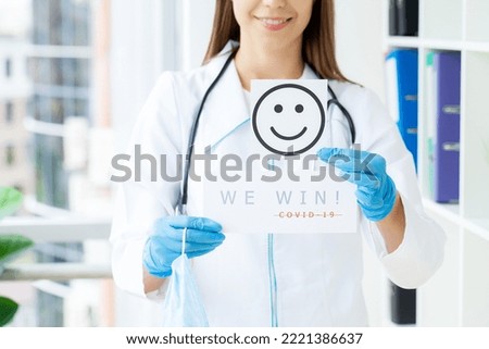 Female doctor in uniform holding a paper signboard lettering we win covid
