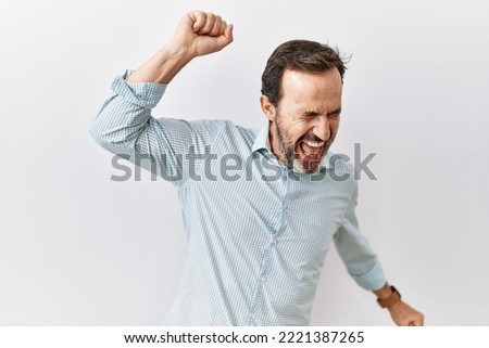 Middle age hispanic man with beard standing over isolated background dancing happy and cheerful, smiling moving casual and confident listening to music  Royalty-Free Stock Photo #2221387265