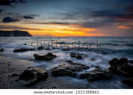 A long exposure seascape of waves washing over rocks on the beach in sunset.