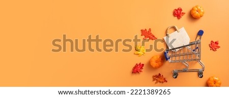 Autumn shopping design concept with shopping cart, maple leaves and pumpkin on orange table background.