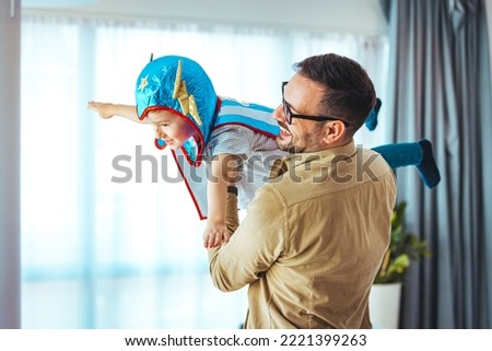 Dream big. Loving father helps his son fly like a superhero. Boy play fly with his dad at home. Cheerful familyare having fun together. Father holding son in superhero costume flying at home 