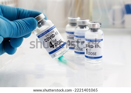 Hand holding COVID-19 Vaccine Vial for vaccination tagged with 4th dose and background 1st, 2nd, 3rd, vaccines. Doctor holding Coronavirus vaccine bottle with name of fourth dose of vaccine on label Royalty-Free Stock Photo #2221401065