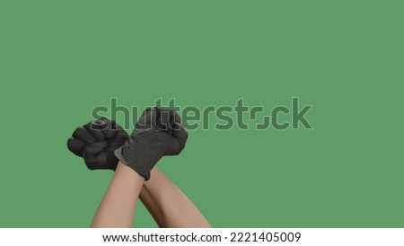 Crossed hands in black gloves with clenched fists raised for protest on green screen. Cropped shot of protester raising arm clenching fist at political demonstration. Concept of revolution or protest.