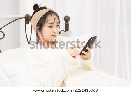 A young woman lying on the bed and operating a smartphone