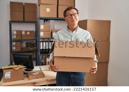 Senior man working at small business ecommerce holding carboard bx smiling looking to the side and staring away thinking. 