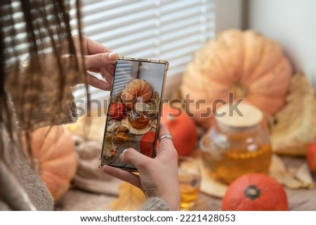 Girl taking photo of pumpkins and autumn leaves on a window. Girl photographing on phone rustic halloween composition. Happy Thanksgiving and Halloween